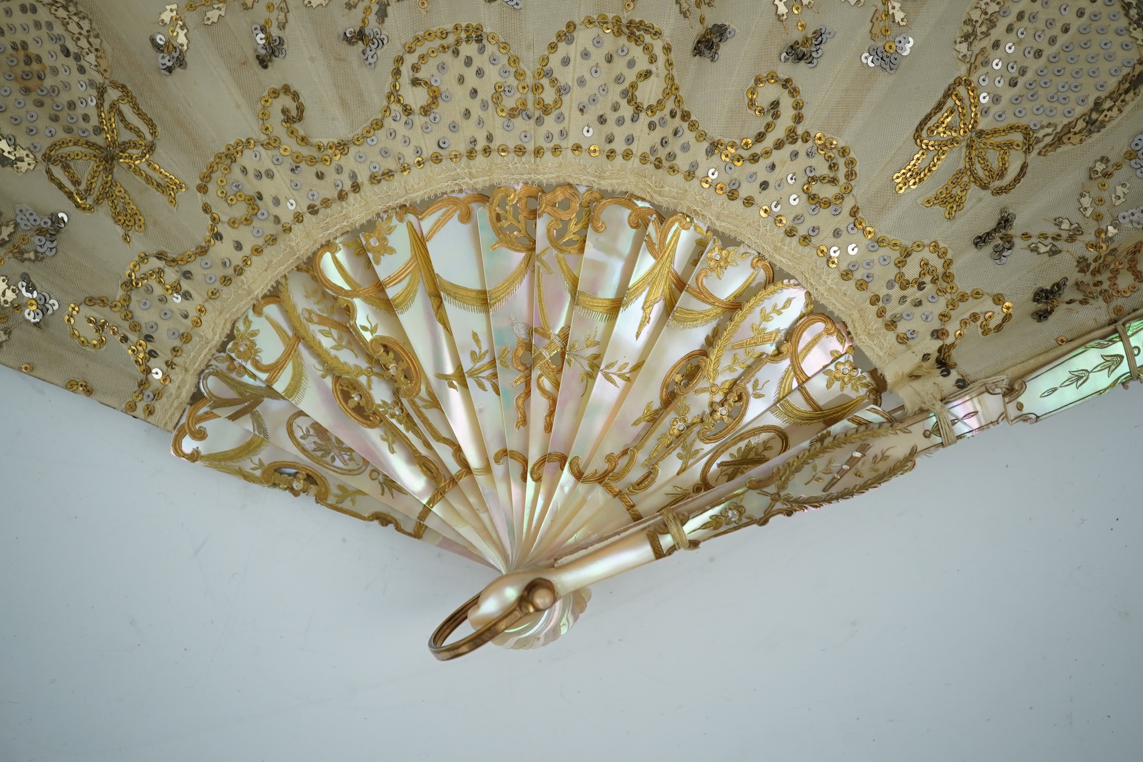 Three French fans: a mother of pearl and sequin fan boxed, a painted silk, feather and bone fan and a gilt decorated bone figural paper fan, the two bone fans having gilt mirrored mounts on the guards, figural paper fan